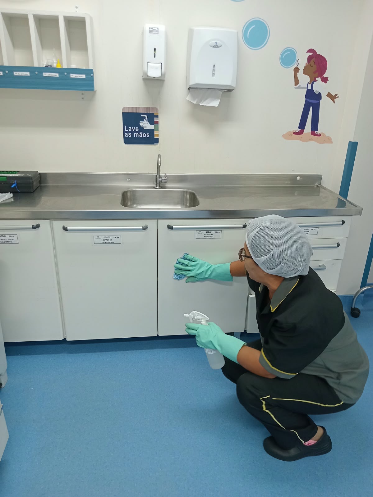 Colaboradora Galileu de uniforme limpando bancada de aço inox em copa de unidade de saúde
